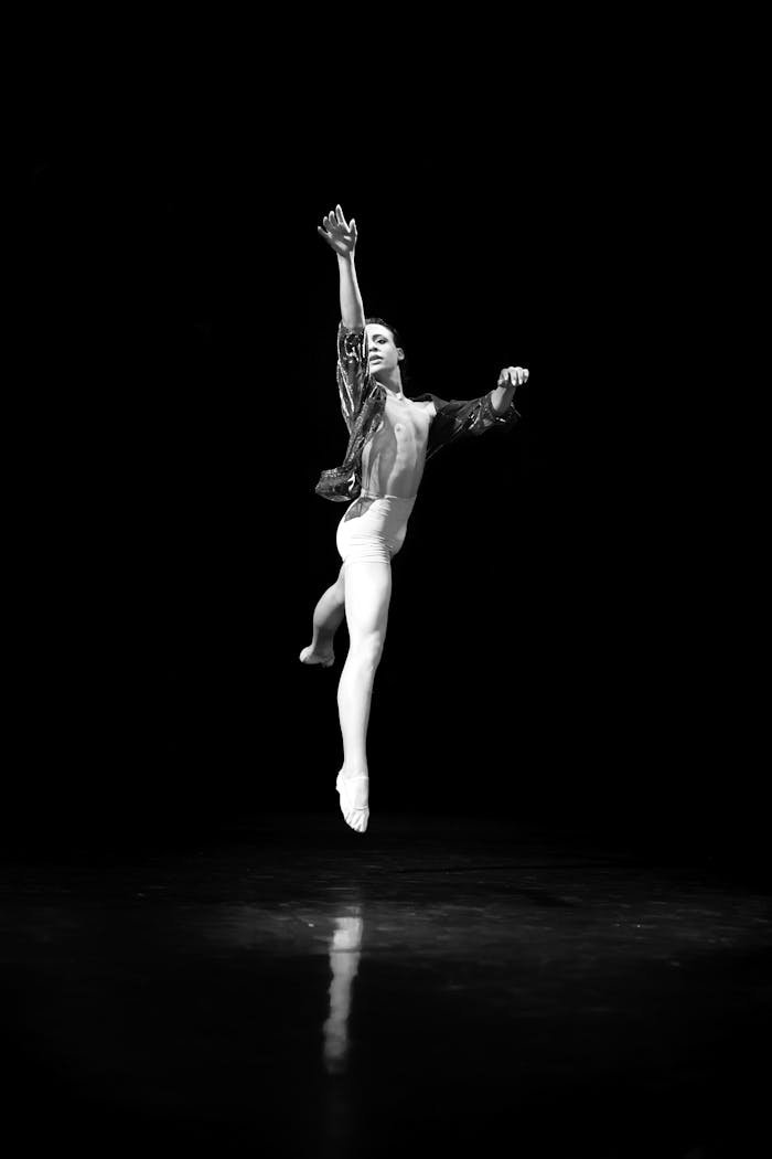 Black and white photo of a male ballet dancer leaping gracefully on stage.