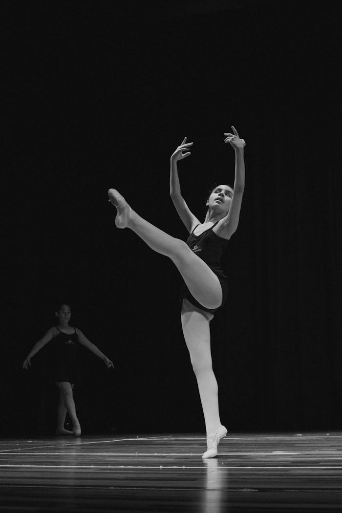 Elegant ballerina performing a high arabesque on stage in a striking black and white scene.